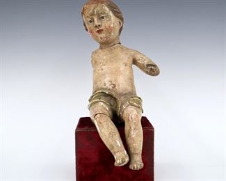 An 18th to 19th century Spanish Colonial creche figure of the Infant Christ. Seated carved wooden figure with polychrome painted detail and inset glass eyes on a later plinth base. Wear and damage, lacks arms. 12 1/2" long. ESTIMATE $100-200