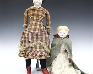 Two 19th century dolls. China heads with molded hair and painted detail, on cloth jointed bodies with leather arms. Includes a doll with Brown painted "flat top" ringlet hair and molded necklace wearing a Brown plaid dress with fringe and leather shoes, and a doll with Blonde painted curly hair wearing a White floral dress with lace, Grey cloak and leather shoes. Minor wear to paint, fabric with some fading, staining and small holes, brunette doll lacks one hand. Up to 26" long. ESTIMATE $100-200