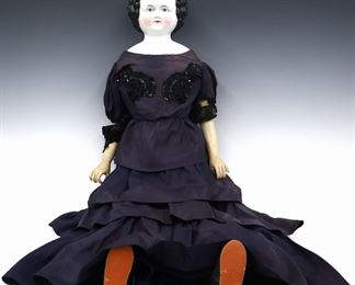 A late 19th century doll. China head with Brown molded "flat top" hair and painted detail, on a later cloth jointed body with composite hands, wearing a Purple gown with sequins and silk shoes. Minor wear to paint, unglazed spot at face, fabric with some fading, staining and small holes. 37" long. ESTIMATE $200-300