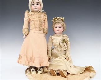 Two turn of the century German dolls. Bisque heads with Blonde hair, open mouths with teeth and painted detail. Includes a full head doll with stationary eyes on a kid jointed body with Bisque lower arms wearing a Peach dress with crochet cap and leather shoes, and a socket head doll with sleep eyes on a jointed composite body wearing a Ivory bridal dress with floral headpiece and leather shoes. Both unmarked. Some wear to paint and composite, one with chipped tooth, fabric with wear, staining and holes. Up to 25" long. ESTIMATE $100-200
