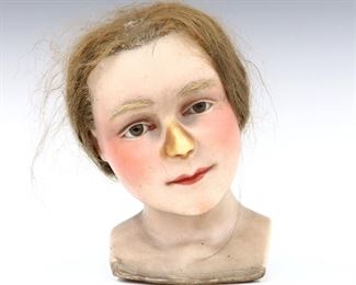 An early 20th century wax mannequin bust. Realistic wax head of a young girl with real Light Brown hair, inset glass eyes, hand-painted lips, and hair eyebrows. Wear and losses, painted finish at nose worn through to wax. 10" high. ESTIMATE $200-400