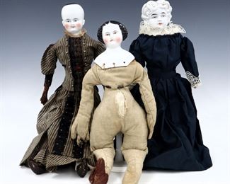 Three 19th century dolls. China heads with painted detail on cloth jointed bodies. Includes a doll with unpainted "flat top" hair wearing a Navy Blue dress, a doll with bare head and leather arms wearing a Brown Victorian dress, and a doll with Brown painted "flat top" hair and no clothing. Some wear to paint particularly to smallest, fabric with some fading, staining and small holes. Up to 21" long. ESTIMATE $100-200
