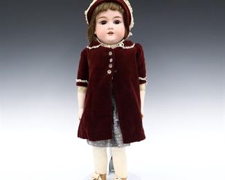 An early 20th century Armand Marseille Model 370 doll. Full bisque head with Light Brown hair, stationary eyes, open mouth with teeth and painted detail on a kid jointed body with porcelain lower arms. Wearing a Blue striped dress with Maroon velvet coat and matching bonnet. Impressed "370 / A.M. 9 DET / Made in Germany" at neck. Minor wear to paint, fabric with minor fading and staining. 23" long. ESTIMATE $100-150