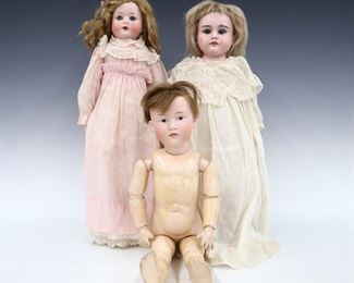 Three turn of the century German dolls. Bisque heads with open mouths and painted detail on jointed composite bodies. Includes an Armand Marseille "Duchess" doll with full head and sleep eyes wearing a White dress in the original box with accessories, a Heubach girl with full head and sleep eyes wearing a Pink dress with lace, and a Heubach boy with socket head and molded eyes without clothing. Impressed marks at necks. Some wear to paint and composite, fabric with wear and fading. Up to 18" long. ESTIMATE $200-300