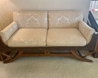 Mid-Century Thai Love Seat. Wooden frame is ornately carved floral front apron and splayed legs.  Ivory Brocade.