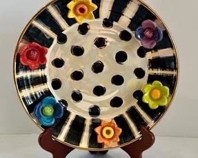 Mary Rose Young Ceramic Decorative Plate with stand. Features a colorful raised floral design with a black and white background accented with gold details. 

Made in England. Measures 10.5” 