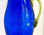 Kosta Boda Art Glass Pitcher, measuring 12”. Gorgeous deep blue pitcher accented with a green art glass handle.