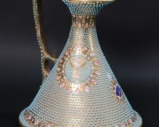 23	Nippon Gilt & Beaded Enamel Porcelain Pitcher	Nippon Japanese export porcelain pitcher. Gilt with turquoise enamel beads and hand painted and enameled armorial decoration. Illegible Nippon mark to the underside. 7"H. Losses to gilt decoration on rim and spout, minor losses to enamel beads and gilt decoration along base.
