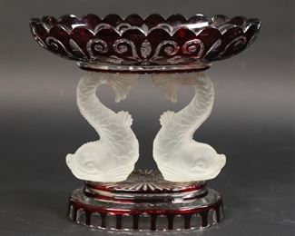 38	Bohemian Glass Ruby Dolphin Compote	Bohemian glass tazza. Color to clear ruby glass, with frosted dolphin form supports. 7 1/4"H x 8 1/4"W. Cracks and chips to plastic hardware on underside, fleabites to dolphins' tails.
