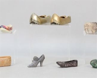 98	Grouping of Asian Miniature Shoe Models	Lot of three pairs and eight single model shoes from various countries in East and South Asia such as China, Korea, Japan, and India. The mediums of the shoes include materials such as stone, ceramic, brass, among others. Three shoes, including one pair and one individual, serve as ash trays while the others appear to be solely decorative. The pair of ash trays measure 5" in length and 1 5/8" in width. All pieces are subject to wear depending on their material such as corrosion, flaking, cracking, chipping, and discoloration.
