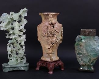 241	3 Chinese Carved Decorative Items	3 Chinese stone carvings. Carved soapstone vase, 14"H; green quartz vase with carved relief scene of woman in landscape (no lid), 8 3/4"H not including collar or wooden base; jade carving of a tree with deer, birds and dragons, on hardstone base, 15 1/4"H including base. Soapstone vase chip to one foot; quartz vase missing lid, minor chips throughout; jade carving as is with chips throughout.
