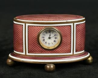 301	Brass & Guilloche Enamel Travel Clock	Guilloche and brass travel / desk clock, probably Austrian. Pink enamel, cobalt painted numerals. 3 3/8"L x 2"H. Losses to patina and tarnishing to brass, screw missing from back of case, chips to enamel along top, base and one side, repair to foot, clock does not appear to be running.
