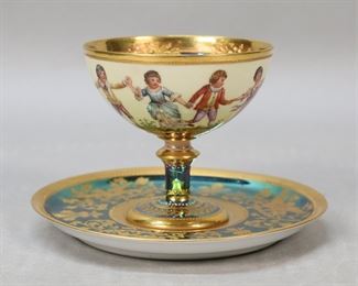 311	Ambrosius Lamm Style Porcelain Sherbet & Saucer	Robert Klemm Dresden German porcelain sherbet, in the style of Ambrosius Lamm. Iridescent green interior, base and stem, with gilt enamel decoration and scene of children playing. Blue Crown RK Dresden mark to the underside. With an associated iridescent green and gilt painted saucer with armorial motif, W in a shield Dresden mark to the underside. Sherbet 3"H, saucer 5 1/4"-diameter. Losses to iridescent glaze on interior of cup and to saucer, losses to gilt on saucer.
