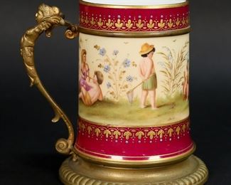 315	Vienna Style Ormolu Mounted Cup	Vienna style porcelain mug. Hand painted scene with children playing, signed Sibl. Gilt painted and enamel decoration, gilt bronze mounts and figural handle. 4 1/4"H. Minor losses to patina on mounts, scratches to magenta ground just below signature.
