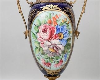 320	Sevres Style Italian Porcelain Urn	Sevres style porcelain urn. Cobalt with hand painted floral decoration and gilt metal mounts. Signed illegibly and marked on the underside Made in Italy Hand Painted 710. 19 1/4"H. Losses and discoloration to patina on mounts.
