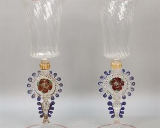 323	Pair of Murano Venetian Glass Goblets	Pair of Murano lampwork glass goblets / wines, both with gilt painted decoration and applied flowers on the stem. Each 13"H. Losses to gilt painted decoration on both, flake to one flower petal.
