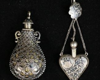 369	2 Silver Scent Bottles Including Russian	2 silver scent / snuff bottles. Hallmarked Russian 84 silver and niello work heart-shaped bottle with chain, bottle 2 3/8"L, 26 grams total; with a scent bottle with scalloped design and enamel lid, unmarked, acid tested as silver, with engraving in Hebrew to neck and base, 4"H, 106 grams total. Losses to enamel on lid of scalloped bottle.
