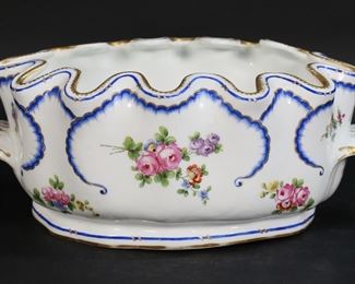 404	Sevres French Porcelain Monteith	Sevres French porcelain wine bottle cooler. Hand painted floral motif, with gilt and cobalt painted decoration. Blue interlaced L mark, D dated mark, circa 1757. 12 1/4"L x 4 7/8"H. Losses to gilt decoration on rim and handles, small chip to one handle.
