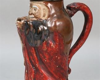 406	Ryosai Sumida Pottery Toby Pitcher	Signed Ryosai Sumida ware Japanese pottery pitcher with lid. Figural "Toby" style form of man with cupped hands as the spout and his hat as the lid. Signed with blue Ryosai seal. 9"H. Paint loss to red decoration throughout, chip to top of handle, vertical firing crack from base into body.
