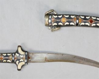 418	Moroccan Koummya Dagger	Moroccan koummya dagger. Inlaid horn, bone, mother of pearl and amber sheath and handle. Curved blade. 15"L (with sheath 15 1/2"L). End missing from sheath, bone inlay missing from sheath and handle, rusting to blade and blade appears to have been re-glued into handle.
