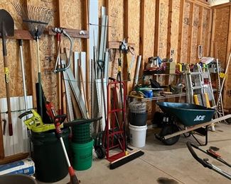 Garage filled with yard and garden tools including ladders, wheelbarrow, blower, rakes, shovels ...