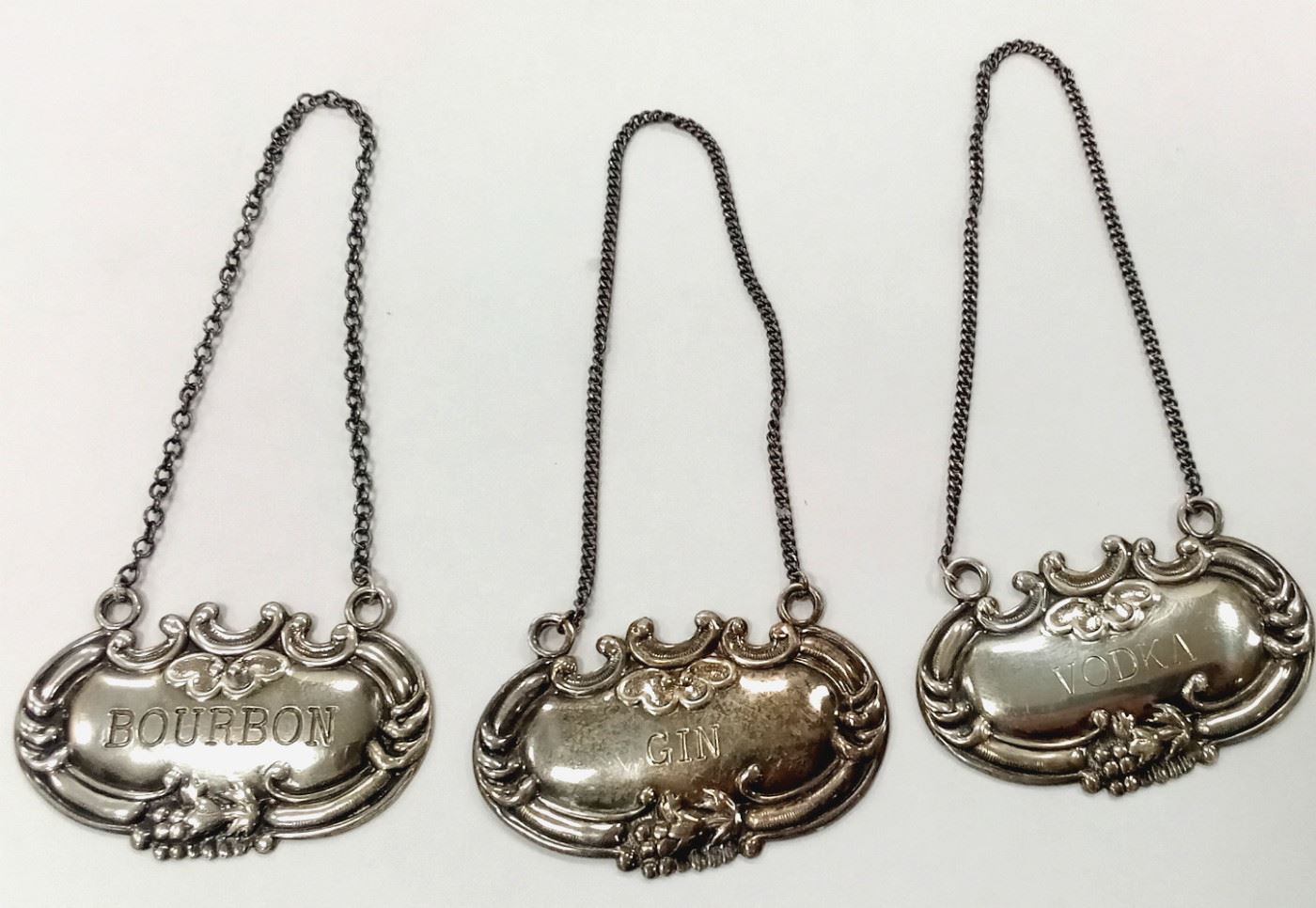 A SET OF THREE WALLACE STERLING LIQUOR BOTTLE TAGS FOR VODKA, BOURBON AND GIN.  2" WIDE.  26.2 GRAMS