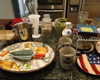 A very fine selection of plates, platters, and cups, and ice bucket, and cookie jars, and red plates in the upper left, and square plate in the middle right, and some other things like that milk glass knobby vase, and then that one thing over on the right.