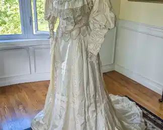 6.)  19th century beaded bridal/wedding gown with Brussels lace, satin, and faux pearls.  Labeled Madam Caryl Artistic Dressmaking. High collar with beads and pearls.  Fancy Ruching.  Brussels lace.  Fancy beadwork at bottom edge of bodice. Bodice is boned.  1 tear in bottom front. Sleeves are trimmed in lace, beads and faux pearls. No underarm stains.  Bodice is in good condition with a couple of tears in the sleeves.  Underskirt - very good condition with a gathered flounce on bottom.  A few pinholes.  Skirt - very delicate with many areas of shattering.  Some staining on train.   Measures:  Bodice:  Shoulder to Shoulder - 14",  Bust - 26",  Waist 24",  Length - 18" to point.  Skirt:  Waist - 24", Length - 43"  Total length  - 61"      $475.00