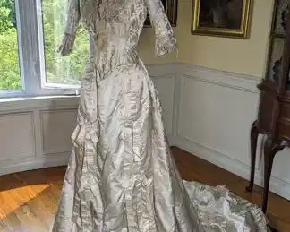 21)  ca 1881  Beaded Brocade Bridal Gown with lace.  Gown is labeled Field Leiter &  Co, Chicago.  Gown is one piece made to look like 2 pieces.  Satin front with bows.  Gown has its own bustle underneath.  Each underarm has a slight stain but no damage.  There is one small tear in the train.  Large train.  Very small size.  According to paperwork when gown was bought, gown is attributed to Alice Sheldon Mathews, Married to Albert Blake Dick of the AB Dick Company on January 25, 1881.  Information will be included with gown.  Gorgeous gown!!  Near Mint Condition.   Measures:  Shoulder to Shoulder  - 11",  Bust 32"-  Waist - 22",  Length 56",  Length with train - 96"    $3400.00