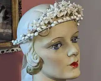 2.) ca 1920's  Wax Floral Bridal/Wedding Crown.  Flowers are mounted on a 2 tier wrapped wire frame.  Wax flowers are orange blossoms with buds.  There are leaves under the flowers.  Satin ribbon hangs from the back.  Wire ring is a little misshaped but can easily be rounded out.  Shorter measurement is 7" diameter.  Excellent condition.              $ 160.00