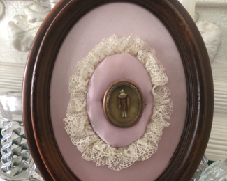 A tiny hand carved and painted, jointed man. Encased in a rolled gold locket/pin, and mounted on pink satin and antique lace, in oval wood frame. Little man is about an inch tall. Exquisite. A real treasure for miniature collectors.