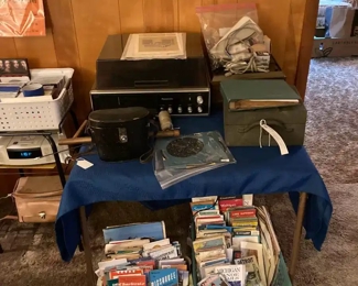 Hand Made Camera Stand; Bushnell Binoculars with Case; Nikkormatt Autofocus Slide Projector, Panasonic Turn Table (with speakers); Vintage and Newer Maps & Tourist Guides; CD's; 1920s Record Player with Bakelite Platter and Set of 10 Birding 45 RPMs.
