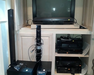 Electronics including subwoofers and soundbars, stereo receiver, VHS player, Cassette player, CD player, and color monitor.