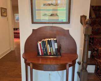 Foyer:  A flip-top game table with center inlay displays an antique book rack with newer books. The art on the wall is a trio of Tuscan drawings.