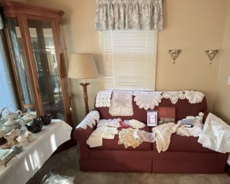 glass curio, floor lamp, red couch, linens and doilies, needlepoint projects, sewing notions