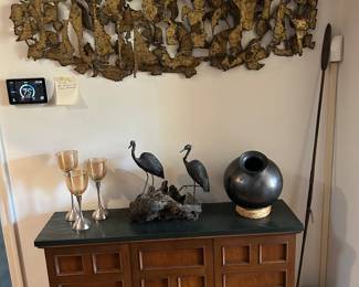 Top to bottom : 1970's Siggi Munk Metal Wall Sculpture measures 57" x 24", 1970's Brutalist Credenza with resin/ slate top measures  46" x 28.5" and 12" D. From R to L: African Metal and Wood Spear in corner,  Vintage Mexican Black Pottery Round Bottom Vase on Straw Stand, Bronze Bird Sculpture attributed to Siggi Munk. 