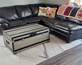 Black Leather Sectional; Oversized Trunk Used as a Coffee Table; Metal Tree Wall Decor; Decorative Pillows; Lap Top Quilt; and Large Area Rug