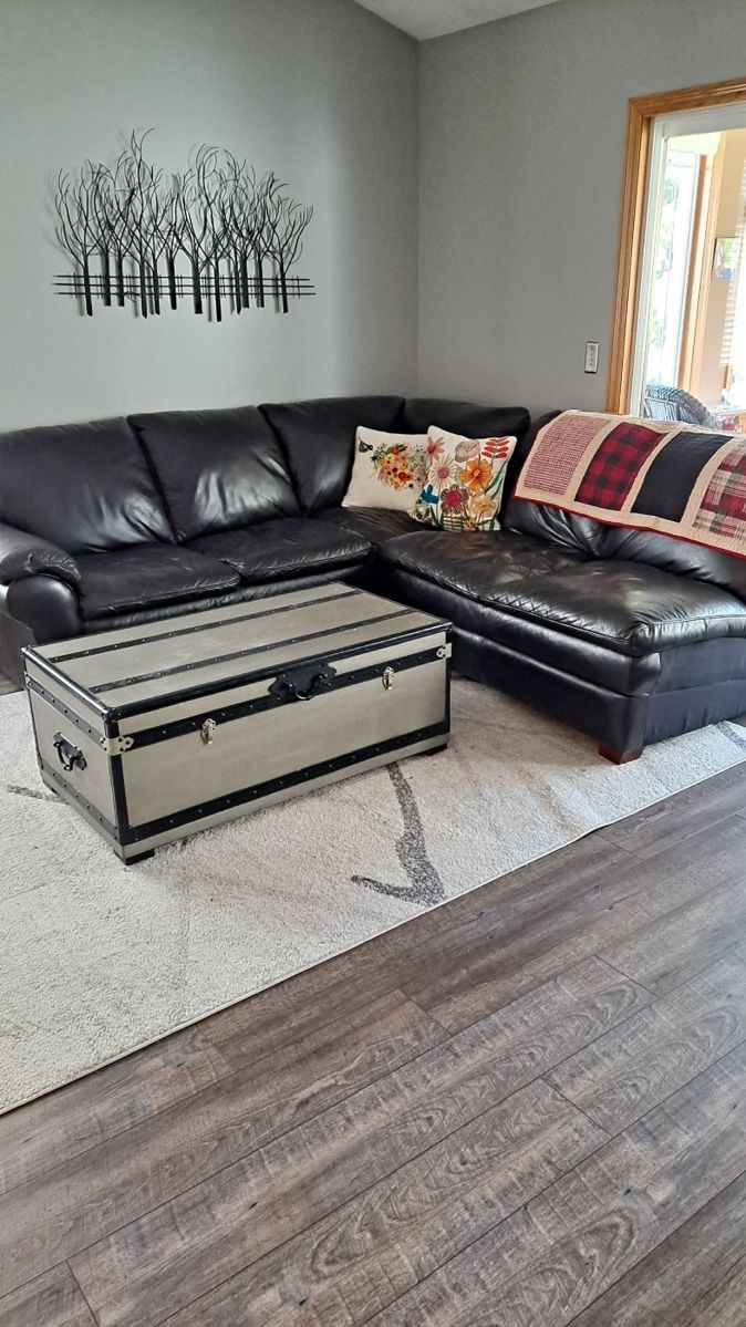Black Leather Sectional; Oversized Trunk Used as a Coffee Table; Metal Tree Wall Decor; Decorative Pillows; Lap Top Quilt; and Large Area Rug