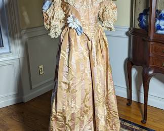 46.)  Ca 1880's Pink and Gold Brocade Reception Gown. Per Wikipedia, "Starting in 1889,[1] Clarkson's company supplied costumes and wigs used in the amateur dramatic productions of Queen Victoria's family and circle.[6] He provided the wigs for the princesses who were attending the fancy-dress Devonshire House Ball of 1897, and visited Buckingham Palace beforehand to arrange their hair.[6]Edward VII appointed him "Royal Perruquier and Costumier."[5]"  William Clarkson was also a Jack the Ripper suspect. Gown is labeled:  W. Clarkson,  Perruquier& Costumer, 41-43 Wardour St, London W.  I cannot read the top of the label,  Royal crest is on the label.   Gown is trimmed in lace and pearls (faux?) and has applied flowers.  Slight shattering under left arm.  Slight train.  A few spots on bodice.  Measures:  shoulder to shoulder 14", Bust 34", Waist 28", Length 58". 