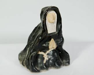 3/4 view of sculpture of a nun wearing a habit, kneeling and praying with a crucifix in her lap