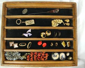 Assorted jewelry in a velvet lined wooden display box (left to right, top to bottom):silver pendant, hat pin, rectangle gold keychain with gemstones in a floral motif, gold feather pin, gold leaf shaped earrings, abstract lavender post earrings, vintage round onyx and gold post earrings, gold dangling earrings, metal square post earrings, oval onyx and gold post earrings, red stone and gold post earrings, gold clip on earrings, gold rectangle hook earrings, two necklaces, polished silver round earrings, cameo earrings.