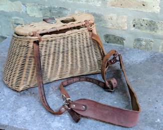 Back view of vintage wicker fishing creel or basket with leather straps and closure