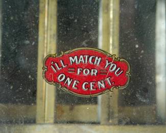 Detail of logo for "I'll Match You for One Cent" antique safety match vending machine