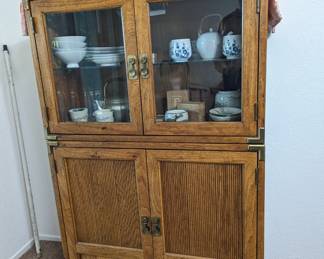 Two-piece Asian style China cabinet. Lighted glass shelf in upper cabinet, wood shelves behind doors below.  All dishware sold separately.