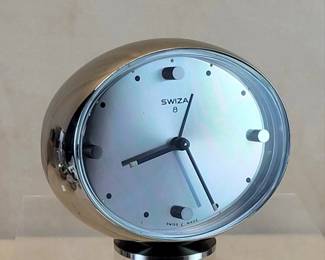 Iconic 1970 Swiza Swiss MCM 8-Day Chrome Alarm Clock.   Modernist example of better mechanical clocks produced just before the battery powered quartz-regulated era.  The chrome plated ovoid case rests at a slight angle on a circular foot with satin brushed top.  Sun-ray machined dial is distinguished by bold applied cylindrical markers at 12, 3, 6 & 9 o'clock.  Black stick hour and minute hands with luminous tips protrude above the slender alarm hand.   

The Swiza 8-day spring driven movement has seven jewels.  Hands set at rear center, above the winding key.  After the alarm is set for wake-up (or whatever!) time, the left knob is pulled out to activate.    

NOTE:  I fully disassembled the movement, ultrasonically cleaned and rinsed all elements, removed the mainspring from the barrel to clean and grease, checked for wear, reassembled and lubricated with high-grade Swiss oil.  $220


