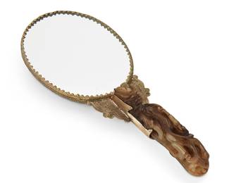 1144
Early/mid-20th century
A Chinese Carved Nephrite Belt Hook Hand Mirror
Appears unmarked
The oval handheld mirror framed by silver-toned metal embossed with foliate and avian motifs, with an inlaid nephrite dragon carved in relief to the verso, and the grip fashioned after an 18th century carved jade belt hook, with a larger dragon's head and smaller dragon's body decorating the handle
9.5" H x 4" W x 1" D
Estimate: $600 - $800