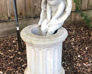 Cast stone cherub seated on a fluted pedestal.