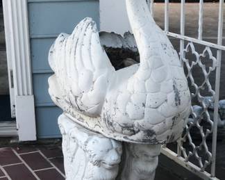 Painted cast metal swan form planter resting on carved marble pedestals.