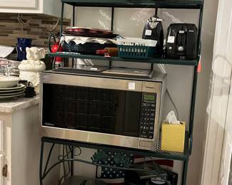 Bakers rack, top shelf 2 green depression glass baking dishes, 2nd shelf-  sunbeam toaster and electric can opener, stack of charger plates, Panasonic microwave, electric skillet, Keurig coffee maker