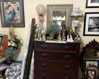 Antique chest of drawers with antique globe lamps, fabric rolls, figurines.